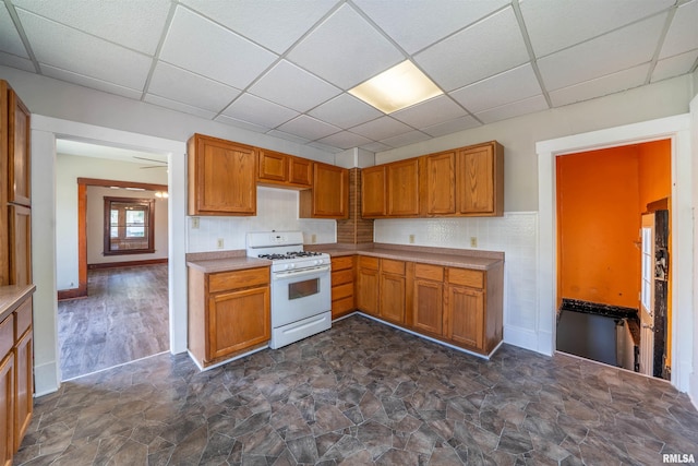 339 Herman St, Pekin, IL 61554 - kitchen featuring a drop ceiling, white range with gas stovetop, brown cabinetry, light countertops, and dark stone finish floors
