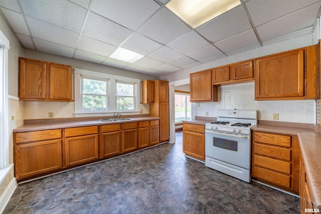339 Herman St, Pekin, IL 61554 - kitchen featuring white gas range oven, a paneled ceiling, brown cabinets, stone finish floors, and backsplash