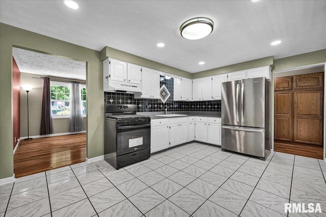 303 W 3rd Ave, Deer Creek, IL 61733 - kitchen with black range with gas cooktop, freestanding refrigerator, white cabinetry, backsplash, and under cabinet range hood