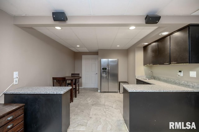 408 W Ravinwoods Rd, Peoria, IL 61615 - kitchen with stainless steel fridge with ice dispenser, a peninsula, recessed lighting, light stone counters, and dark brown cabinetry