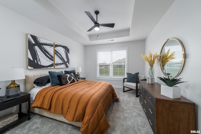 carpeted bedroom featuring ceiling fan and a tray ceiling