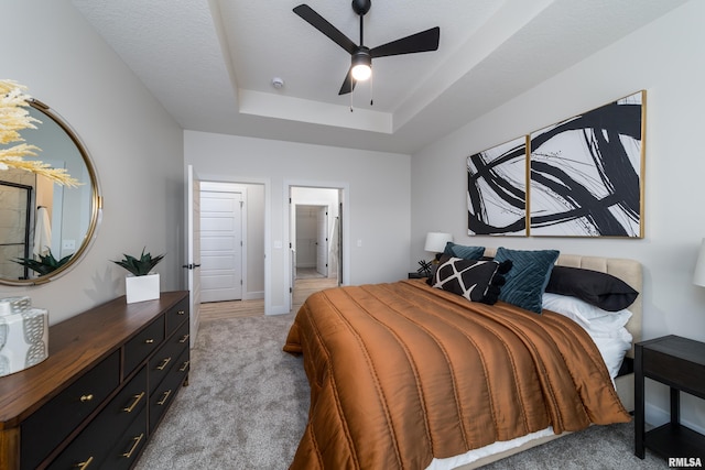 bedroom with a textured ceiling, light colored carpet, ceiling fan, and a raised ceiling