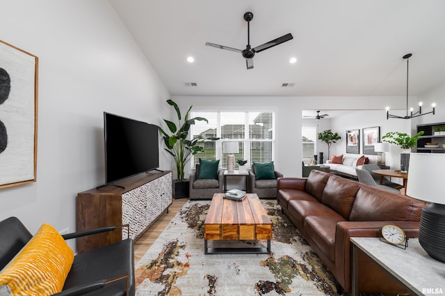 living room with ceiling fan with notable chandelier, light hardwood / wood-style floors, and vaulted ceiling