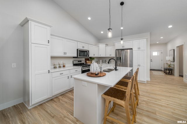 kitchen with stainless steel appliances, decorative light fixtures, an island with sink, white cabinets, and light hardwood / wood-style flooring