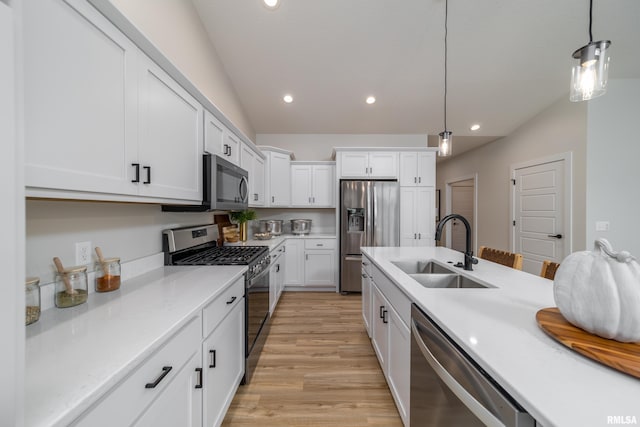 kitchen with white cabinetry, appliances with stainless steel finishes, hanging light fixtures, sink, and light hardwood / wood-style floors