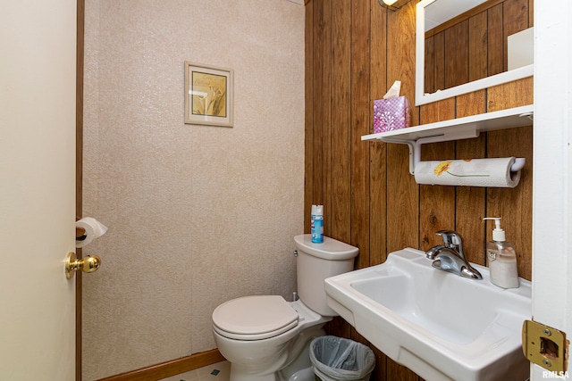 bathroom with toilet, wood walls, and sink