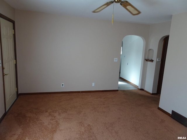 spare room with arched walkways, carpet floors, ceiling fan, and baseboards