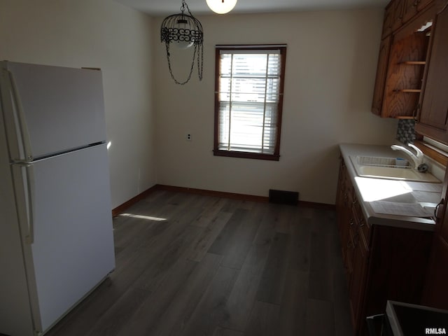 kitchen with baseboards, wood finished floors, freestanding refrigerator, light countertops, and a sink