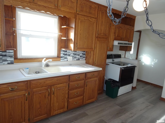 kitchen with brown cabinets, a sink, under cabinet range hood, and white range with electric cooktop