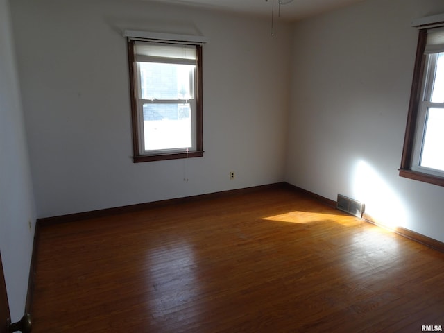 empty room featuring wood finished floors, visible vents, and baseboards