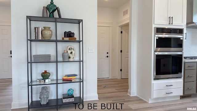 interior space with visible vents, backsplash, double oven, light wood-style floors, and white cabinets