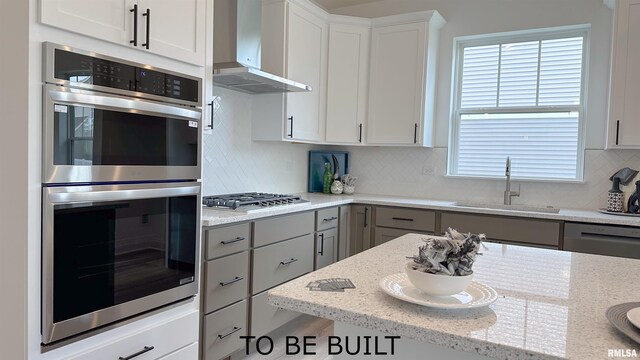 kitchen with wall chimney exhaust hood, a sink, stainless steel appliances, gray cabinetry, and backsplash