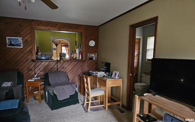 carpeted home office featuring ceiling fan, ornamental molding, and wooden walls