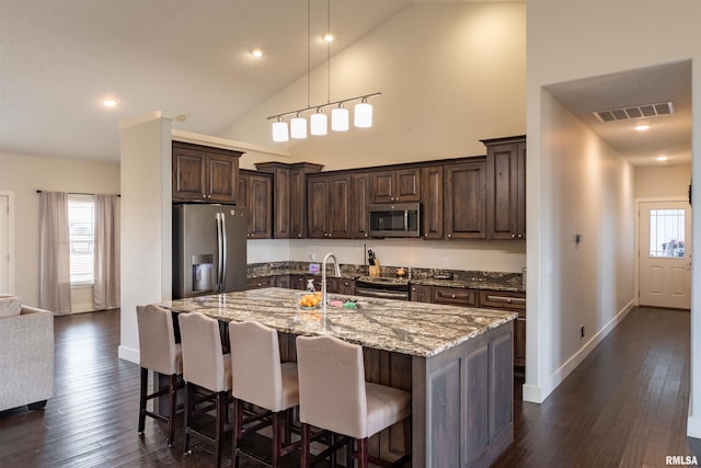 kitchen featuring stainless steel appliances, high vaulted ceiling, decorative light fixtures, light stone countertops, and dark wood-type flooring