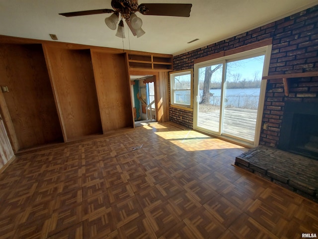 unfurnished living room featuring ceiling fan, a water view, brick wall, and dark parquet flooring