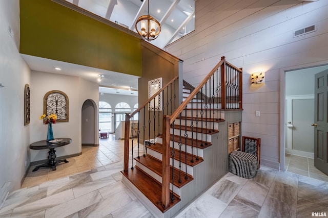 staircase featuring a chandelier, light tile flooring, wooden walls, and a towering ceiling