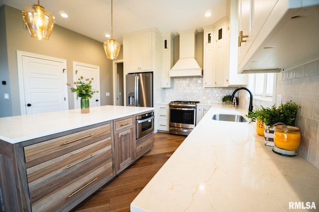 kitchen with appliances with stainless steel finishes, custom range hood, sink, white cabinets, and hanging light fixtures