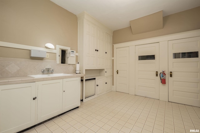 kitchen featuring sink, tasteful backsplash, light tile floors, and white cabinetry