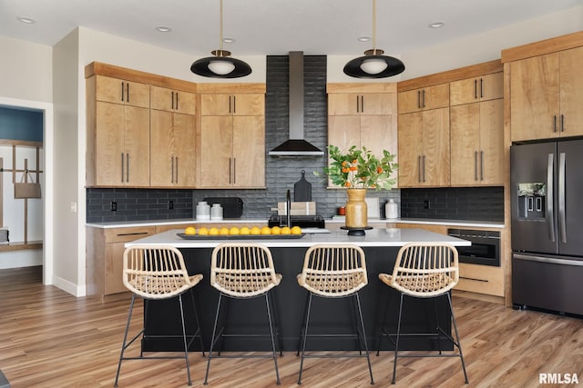 kitchen featuring wall chimney range hood, stainless steel fridge with ice dispenser, backsplash, and an island with sink