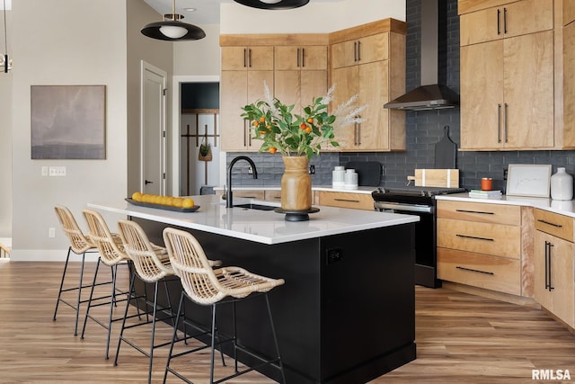 kitchen featuring backsplash, black range oven, a center island with sink, wall chimney range hood, and sink