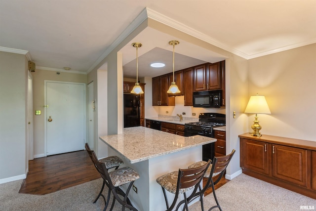 kitchen with hanging light fixtures, black appliances, light stone counters, hardwood / wood-style floors, and a kitchen bar