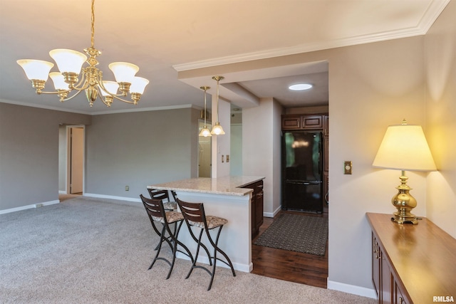 kitchen featuring a breakfast bar area, black refrigerator, hanging light fixtures, ornamental molding, and hardwood / wood-style flooring