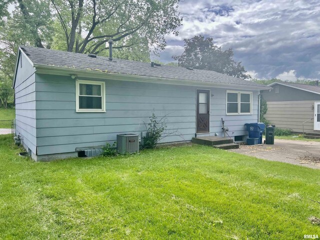 rear view of property featuring a shingled roof, central AC, and a yard