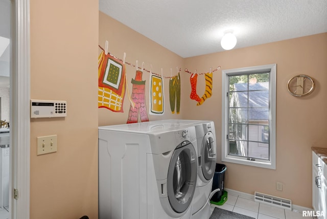 washroom with a textured ceiling, washing machine and dryer, and light tile patterned floors