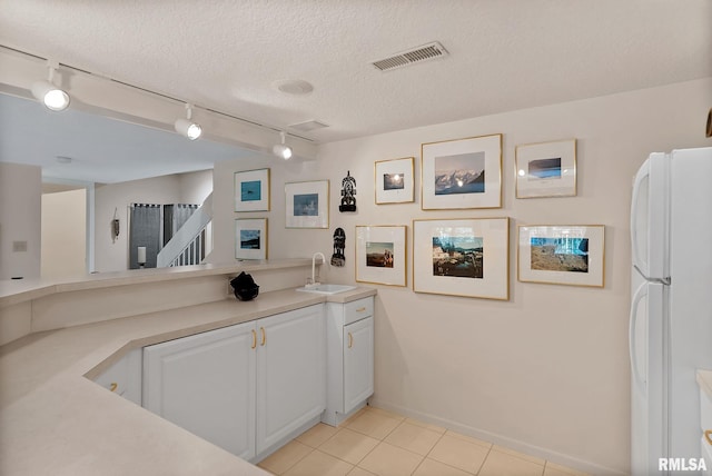 kitchen featuring track lighting, sink, a textured ceiling, white fridge, and white cabinetry