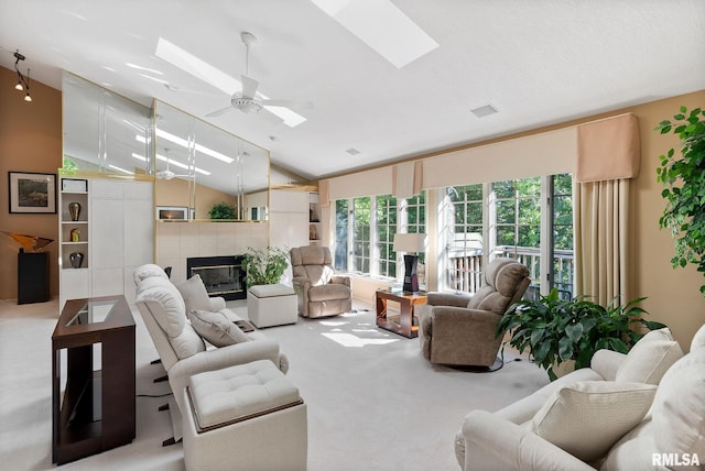 carpeted living room featuring a tile fireplace, ceiling fan, and vaulted ceiling with skylight