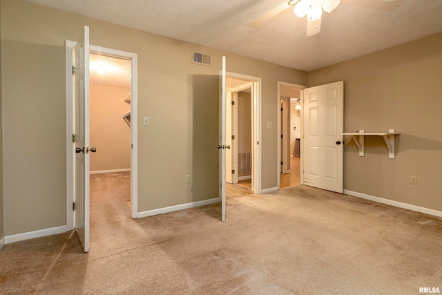 unfurnished bedroom featuring ceiling fan, light colored carpet, a textured ceiling, and a walk in closet