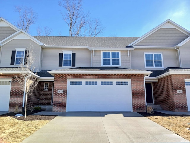 townhome / multi-family property with a garage, brick siding, driveway, and roof with shingles