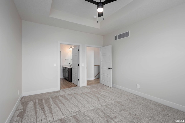 unfurnished bedroom with light carpet, ensuite bathroom, and ceiling fan