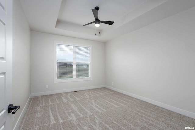 spare room with a raised ceiling, light carpet, and ceiling fan