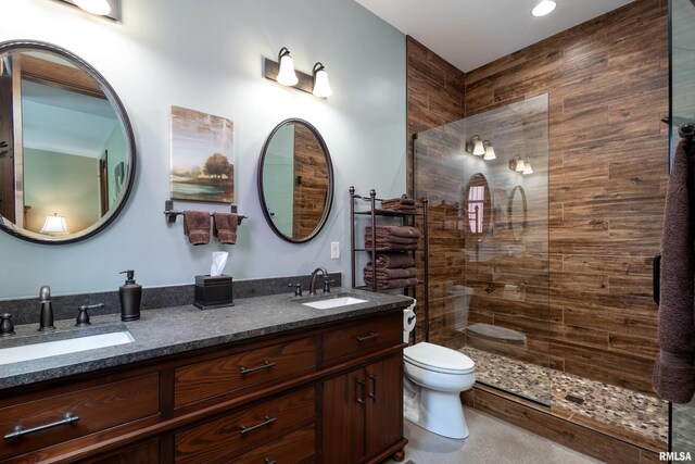 bathroom with a tile shower, dual vanity, and toilet