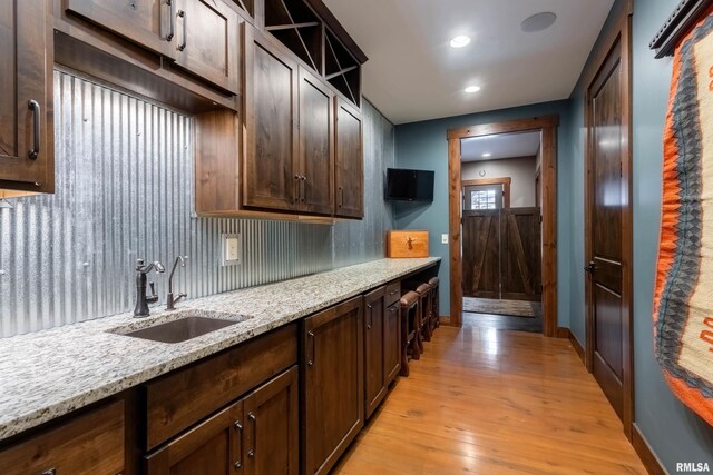 kitchen with sink, light stone countertops, dark brown cabinetry, and light hardwood / wood-style flooring