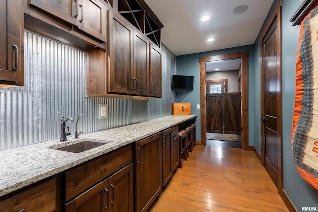 kitchen with light wood-style flooring, light stone counters, open shelves, and a sink