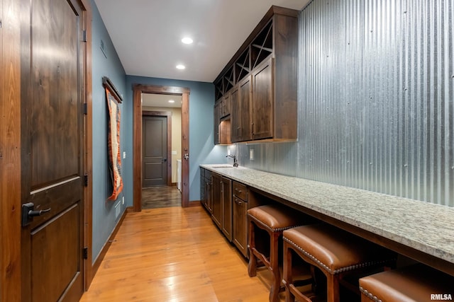 kitchen featuring a kitchen breakfast bar, light hardwood / wood-style flooring, light stone counters, dark brown cabinetry, and sink