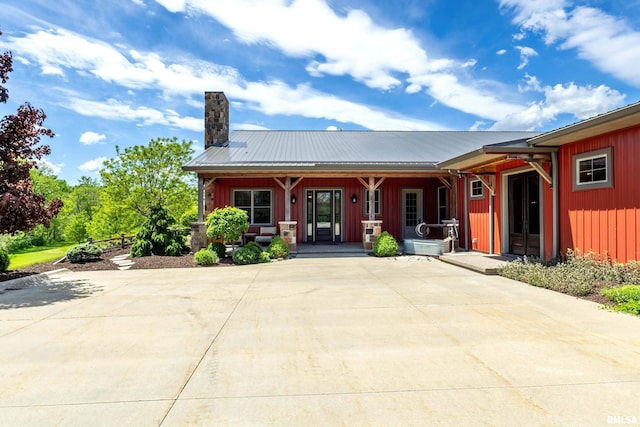 view of front facade with metal roof, a chimney, a porch, and board and batten siding