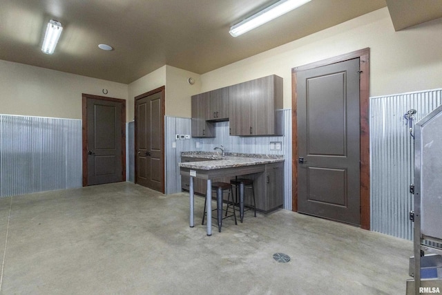 kitchen featuring a breakfast bar, concrete floors, a sink, light countertops, and wainscoting