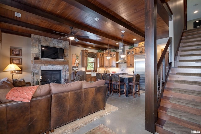 living room featuring ceiling fan, a stone fireplace, wood ceiling, beamed ceiling, and sink