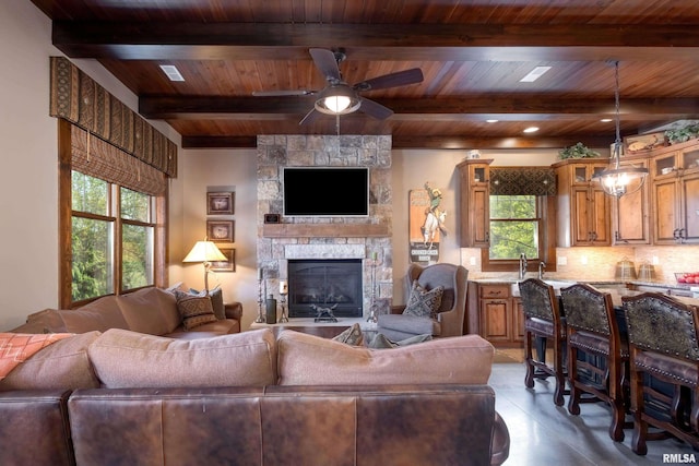 living room featuring beamed ceiling, ceiling fan, a fireplace, and wood ceiling