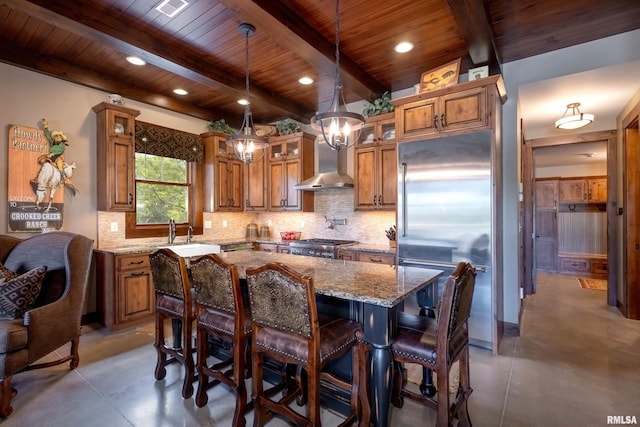 kitchen featuring light stone countertops, backsplash, a kitchen island, wall chimney exhaust hood, and built in refrigerator