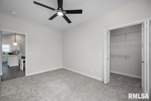 unfurnished bedroom with dark colored carpet, a spacious closet, ceiling fan, and a closet