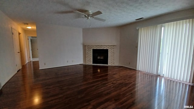 unfurnished living room featuring ceiling fan, dark wood-type flooring, a textured ceiling, and a brick fireplace