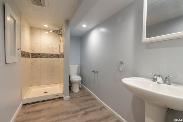 bathroom featuring tiled shower, toilet, and wood-type flooring