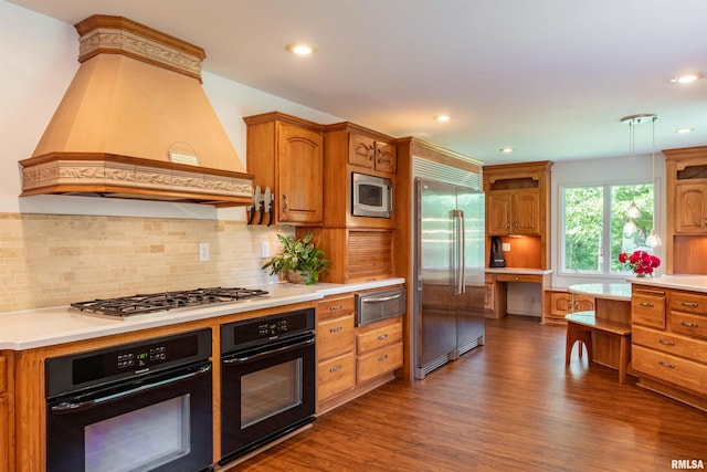 kitchen with premium range hood, built in appliances, hanging light fixtures, dark hardwood / wood-style floors, and decorative backsplash