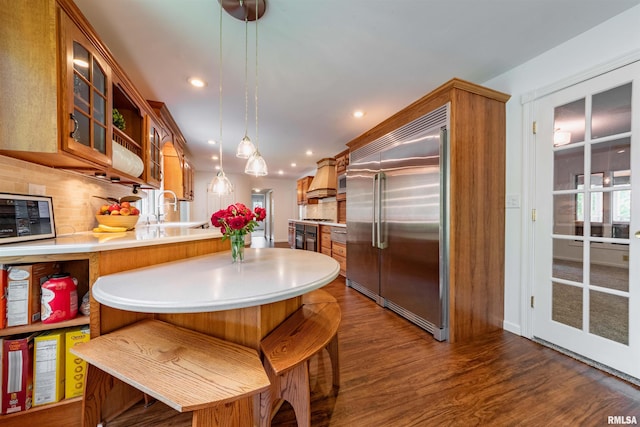 kitchen featuring dark wood-type flooring, built in appliances, a kitchen bar, decorative light fixtures, and kitchen peninsula