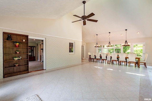 living room with light tile patterned floors, ceiling fan with notable chandelier, high vaulted ceiling, and brick wall