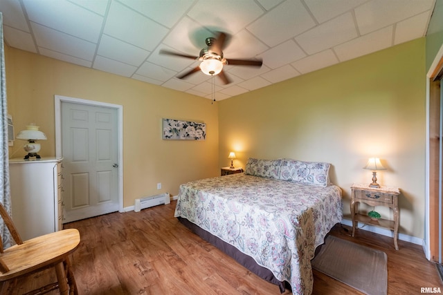 bedroom featuring wood-type flooring, a baseboard heating unit, a paneled ceiling, and ceiling fan